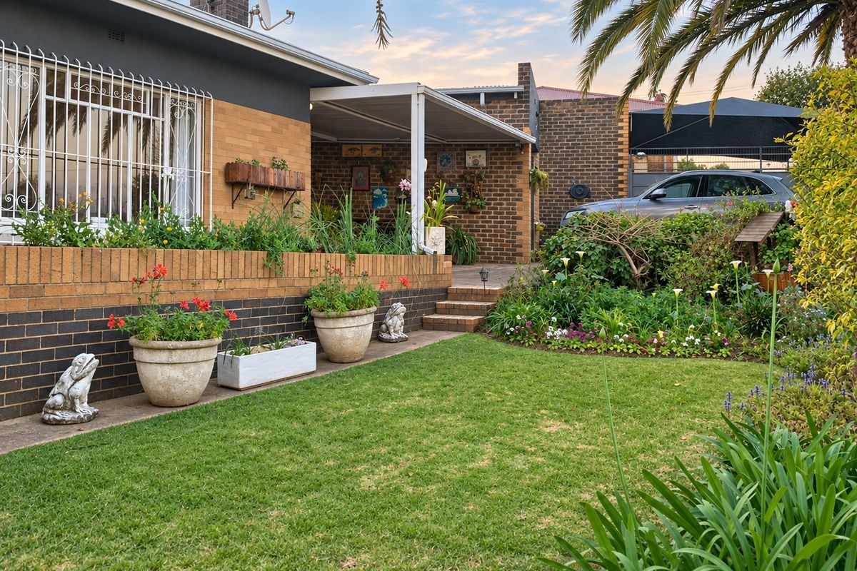 A well-maintained rear garden featuring a brick facade, a covered patio area, and a neatly landscaped lawn with established garden beds.