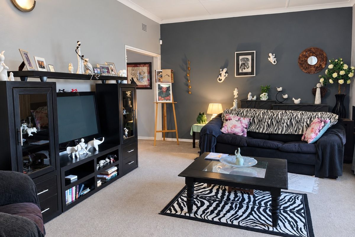 A comfortable living room featuring neutral and dark accent walls, carpeted flooring, and decorative coving.