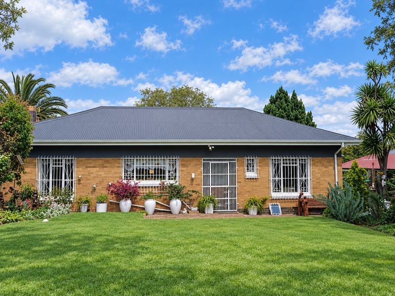 A well-maintained rear exterior view of a brick house featuring a modern corrugated metal roof, security bars on windows, and a neat lawn.