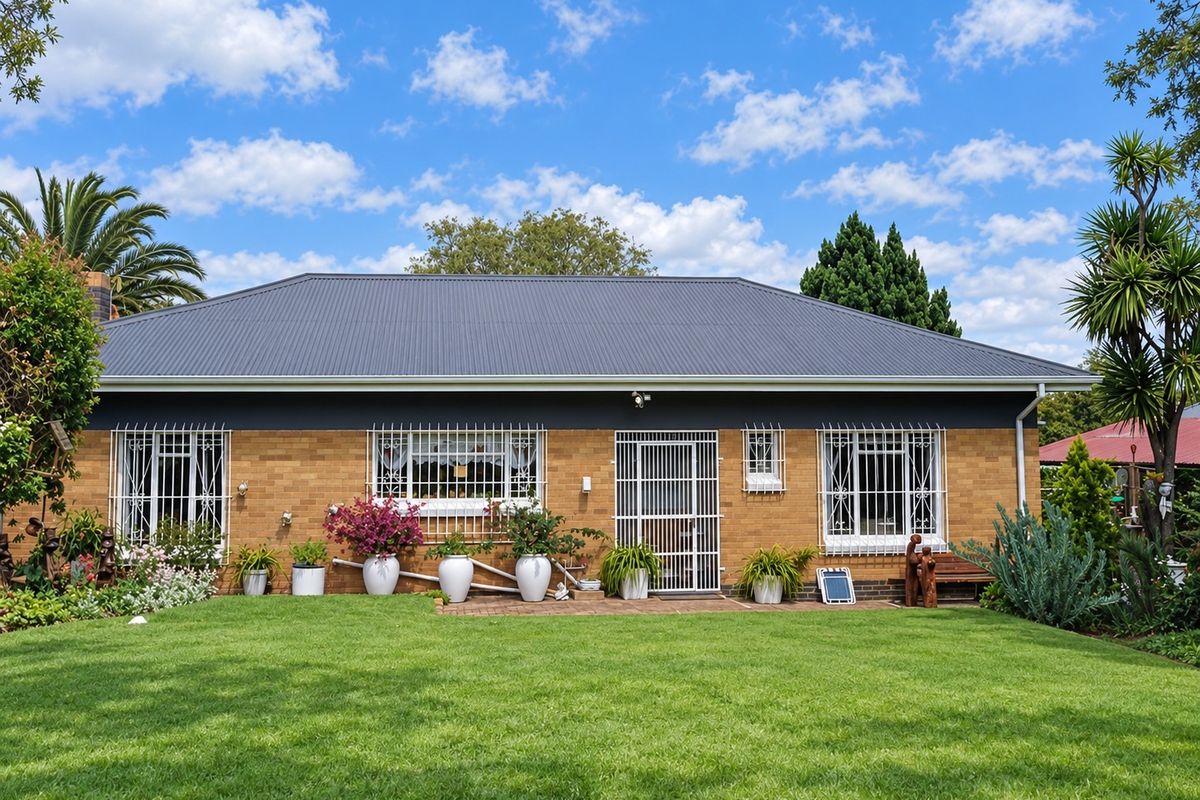 A well-maintained rear exterior view of a brick house featuring a modern corrugated metal roof, security bars on windows, and a neat lawn.