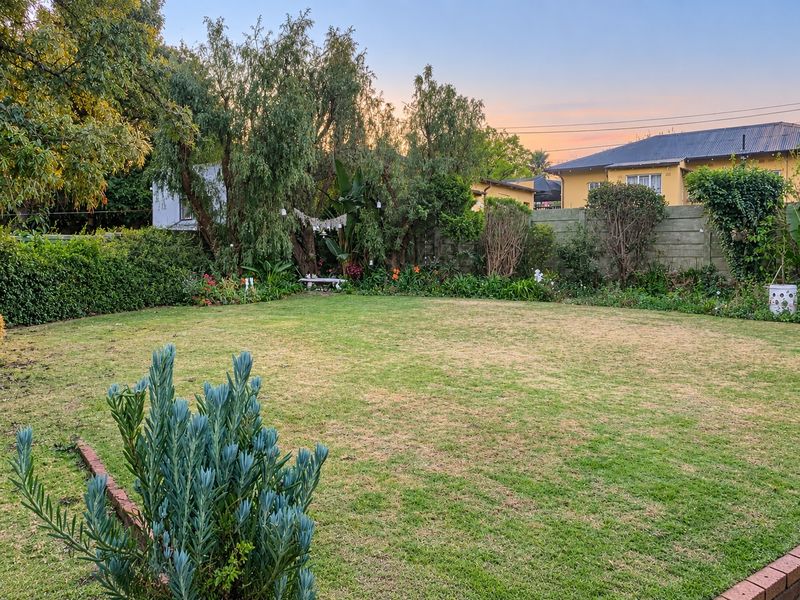 A spacious, well-established rear garden featuring a large lawn, mature trees, and perimeter walling, providing a private outdoor space.