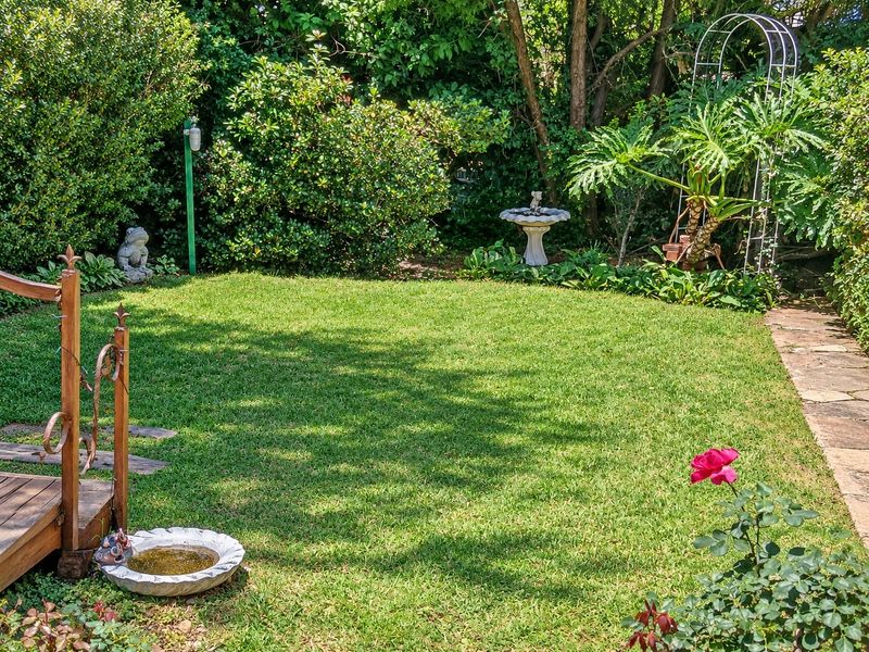 A well-maintained private garden featuring a lush green lawn, mature perimeter hedging, and a stone pathway leading through the landscaped outdoor space.