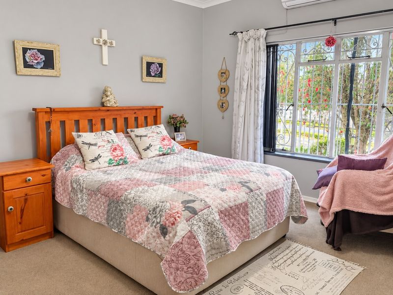 A well-maintained bedroom featuring neutral walls, carpeted flooring, and a large window with security bars and an integrated air conditioning unit.