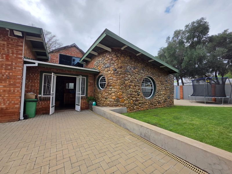 Rear exterior view featuring a unique stone-clad section with circular windows, brick walls, and a paved patio area leading to the garden.