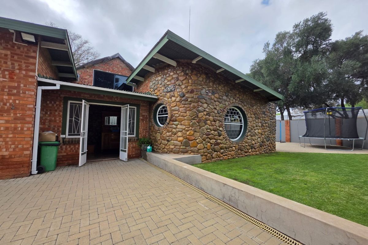 Rear exterior view featuring a unique stone-clad section with circular windows, brick walls, and a paved patio area leading to the garden.