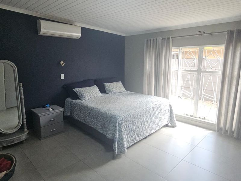 Spacious bedroom featuring tiled flooring, a split-system air conditioner, and a sliding glass door with security gate providing access to the exterior.
