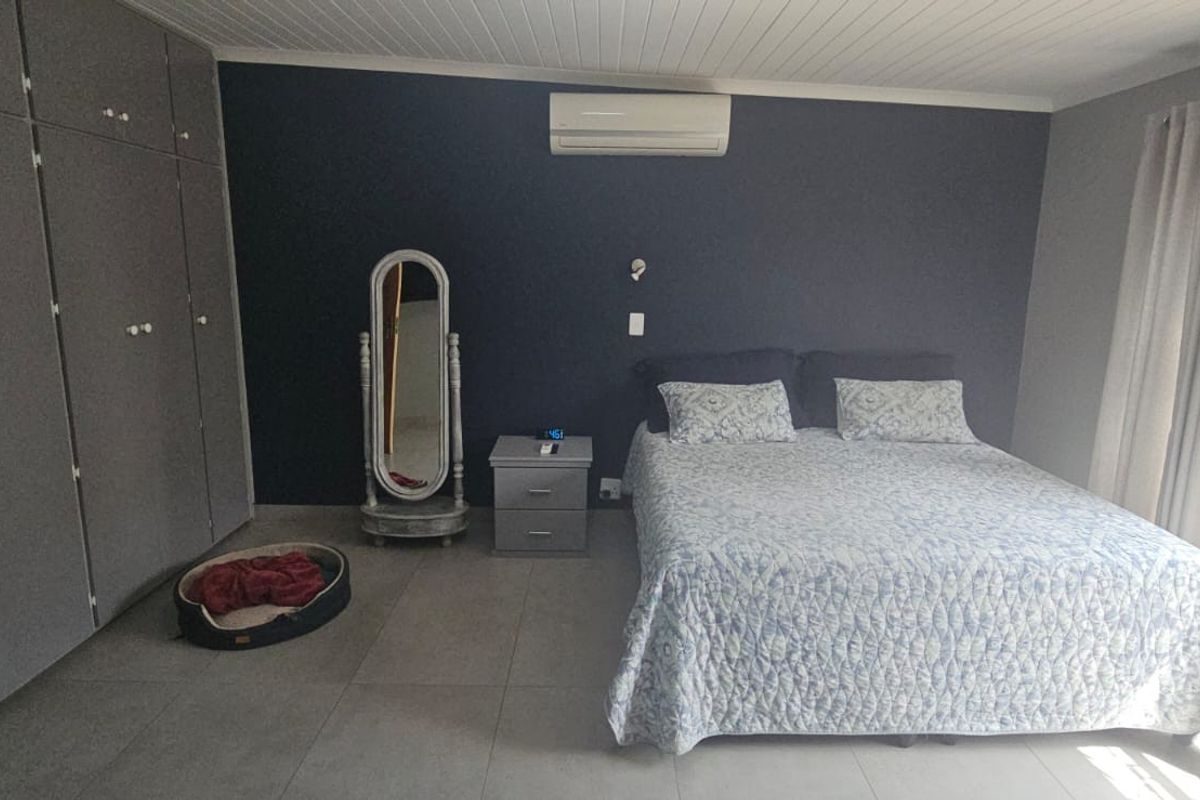 Spacious bedroom featuring built-in cupboards, tiled flooring, a tongue and groove ceiling, and a wall-mounted air conditioning unit.