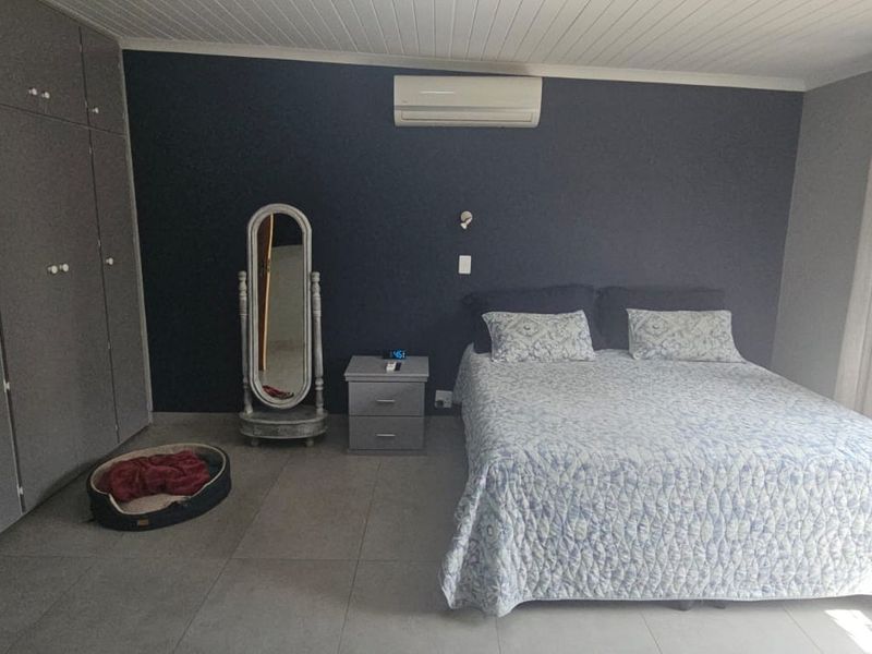 Spacious bedroom featuring built-in cupboards, tiled flooring, a tongue and groove ceiling, and a wall-mounted air conditioning unit.