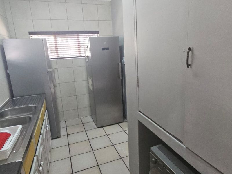 A functional laundry room featuring tiled walls and flooring, a double stainless steel sink, and built-in storage cabinetry.