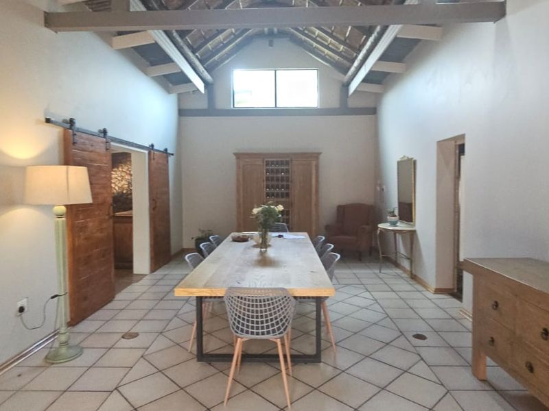 Spacious dining room featuring high vaulted ceilings with exposed timber trusses, tiled flooring, and rustic sliding barn doors.