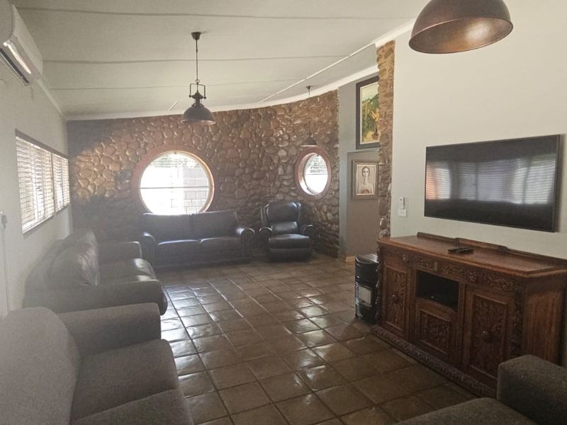 Spacious living room featuring a distinctive stone feature wall, circular windows, tiled flooring, and a wall-mounted air conditioning unit.
