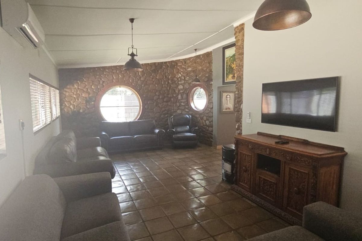 Spacious living room featuring a distinctive stone feature wall, circular windows, tiled flooring, and a wall-mounted air conditioning unit.