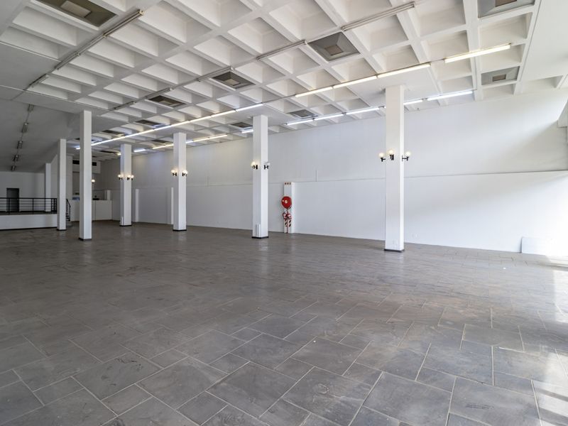 Spacious open-plan commercial area featuring a distinctive waffle slab ceiling, structural columns, and durable stone tile flooring, suitable for various business applications.