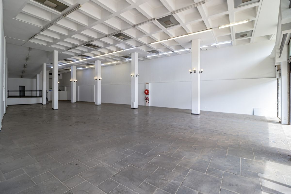 Spacious open-plan commercial area featuring a distinctive waffle slab ceiling, structural columns, and durable stone tile flooring, suitable for various business applications.