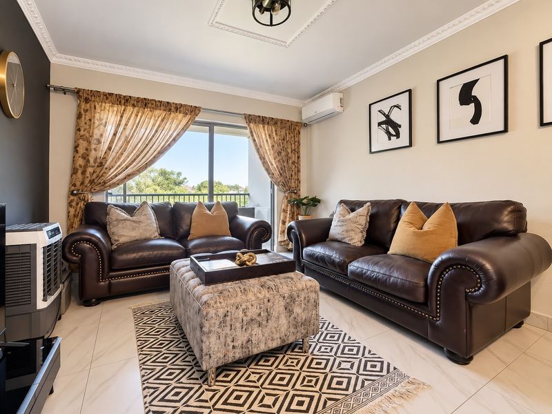 A well-maintained living room featuring crown molding, a ceiling rose, tiled flooring, and a sliding glass door leading to a balcony.