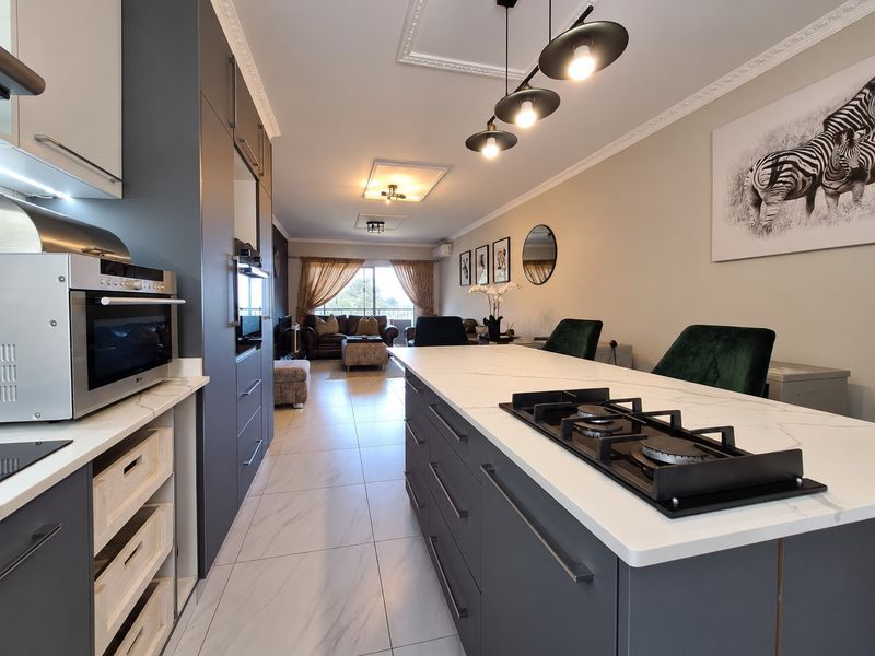 Modern open-plan kitchen and living area featuring a central island with gas hob, sleek cabinetry, and high-quality tiled flooring throughout.