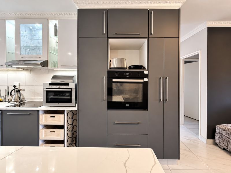 Modern kitchen featuring sleek dark cabinetry, built-in oven, extractor fan, marble-look countertops, and elegant crown molding with tiled flooring.