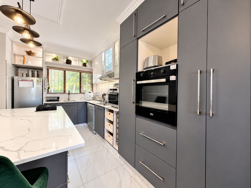 Modern kitchen featuring sleek grey cabinetry, a large quartz-topped island, built-in oven, gas hob, and elegant crown molding with high-quality finishes.