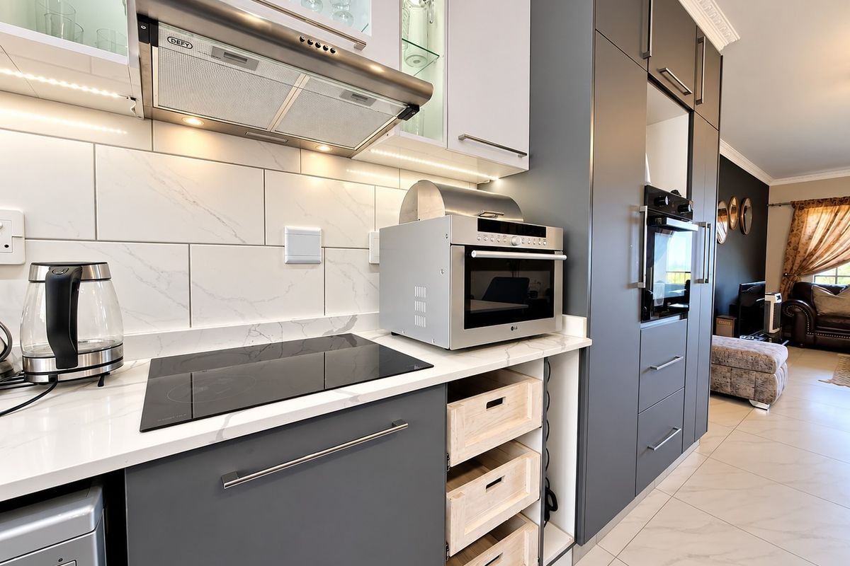 Modern kitchen featuring sleek grey cabinetry, marble-look countertops, subway tile backsplash, integrated oven, and high-quality porcelain floor tiles.