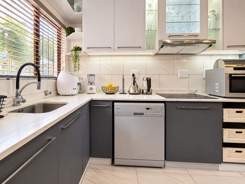 Modern kitchen featuring sleek grey and white cabinetry, stone countertops, marble-look backsplash, integrated appliances, and high-quality finishes throughout.