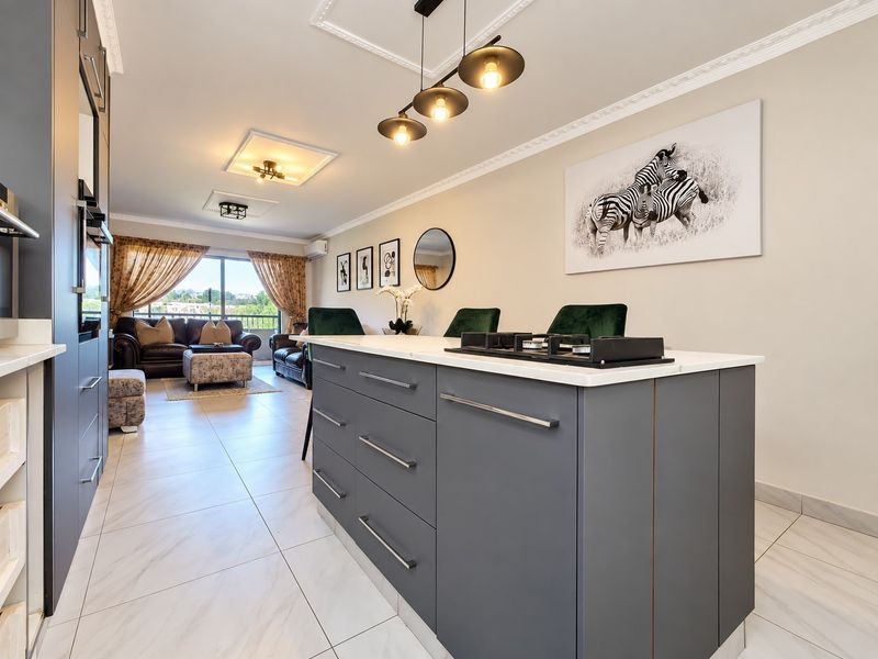 Modern open-plan living area featuring a sleek kitchen island with integrated gas hob, tiled flooring, and elegant ceiling detailing leading to a balcony.