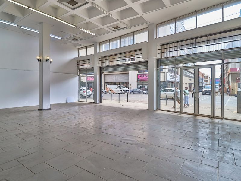 Spacious open-plan commercial retail space featuring high coffered ceilings, large glass storefront windows, and durable stone tile flooring.