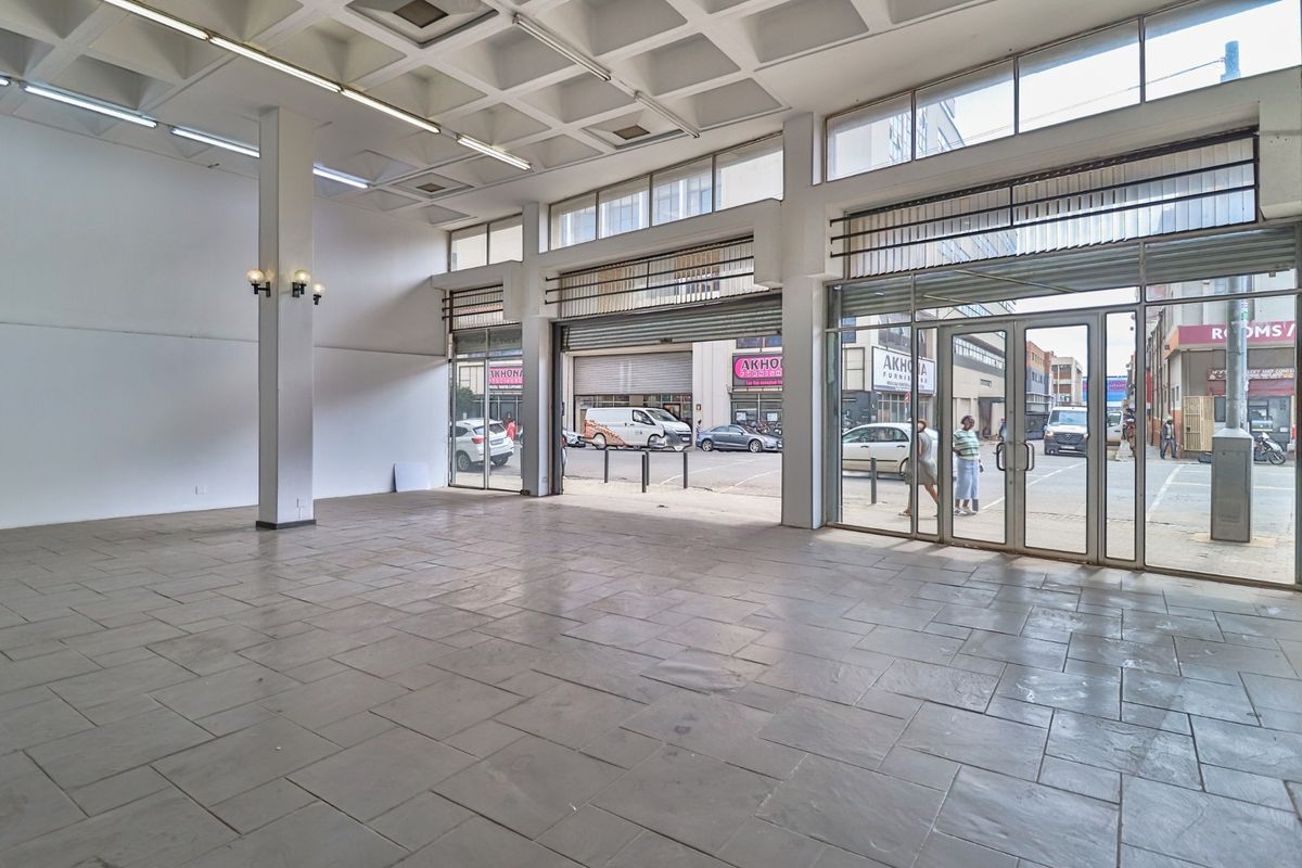 Spacious open-plan commercial retail space featuring high coffered ceilings, large glass storefront windows, and durable stone tile flooring.