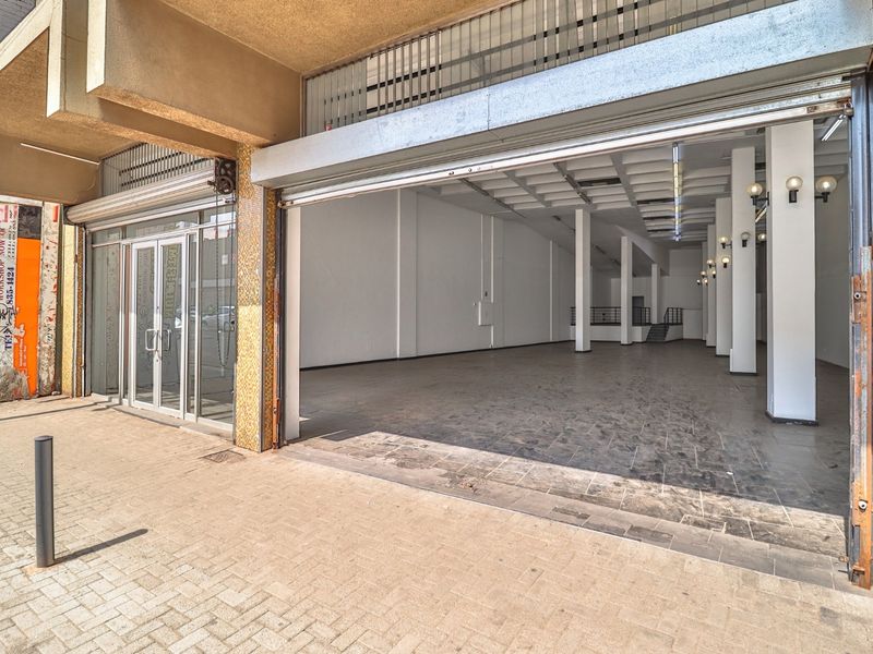 Commercial storefront featuring a large roller shutter door, glass entrance, and an open-plan interior with concrete columns and tiled flooring.