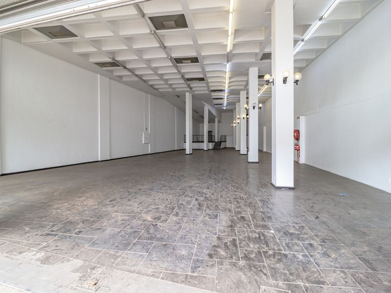 A spacious, empty commercial open-plan area featuring a distinctive waffle slab ceiling, structural columns, and durable stone tile flooring.