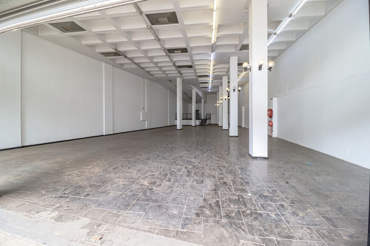 A spacious, empty commercial open-plan area featuring a distinctive waffle slab ceiling, structural columns, and durable stone tile flooring.