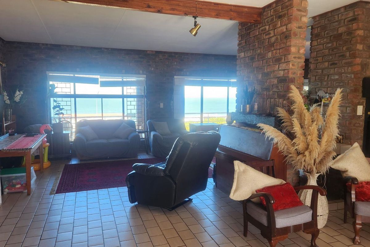 Spacious living area featuring exposed brick walls, tiled flooring, a built-in fireplace, and large sliding doors offering scenic coastal views.