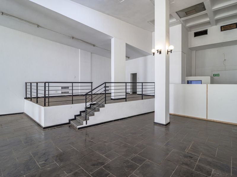 Spacious open-plan commercial interior featuring a raised platform, structural columns, and tiled flooring, suitable for a versatile retail or office layout.