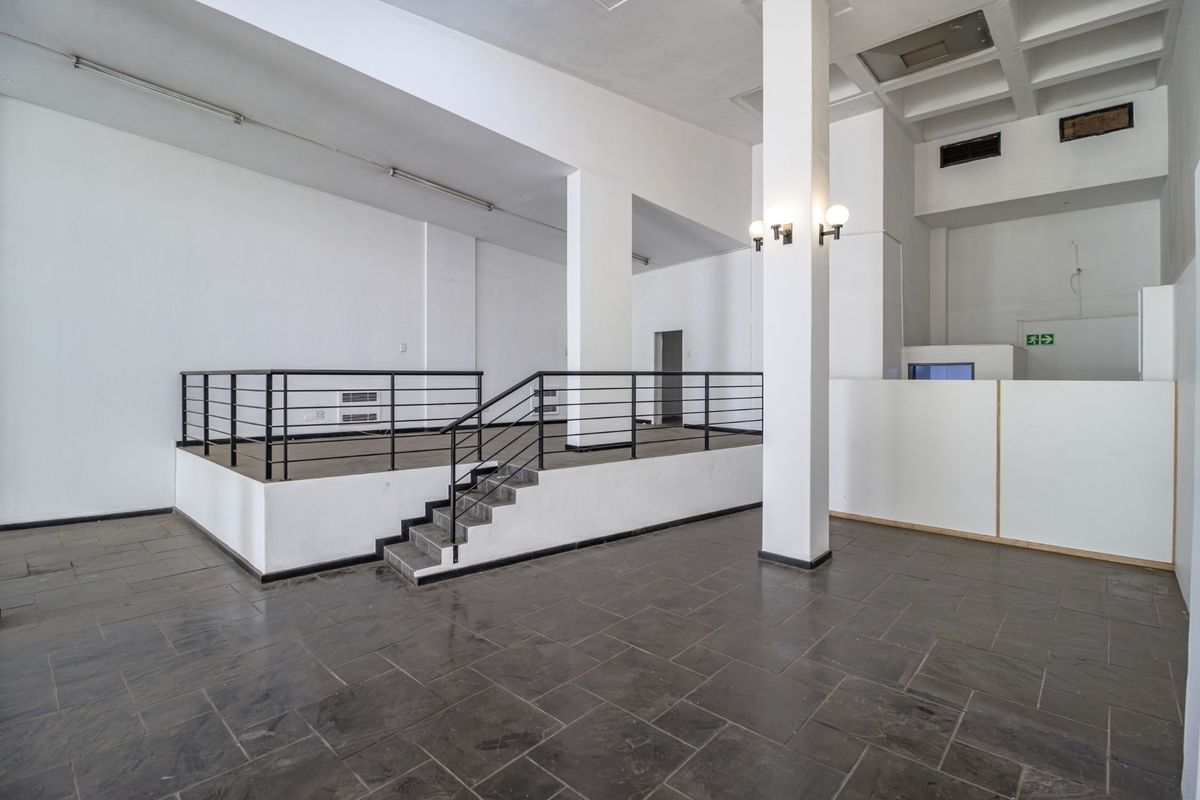 Spacious open-plan commercial interior featuring a raised platform, structural columns, and tiled flooring, suitable for a versatile retail or office layout.