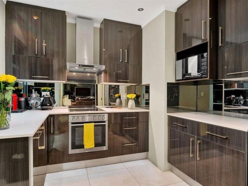 Modern kitchen featuring dark wood-grain cabinetry, stone countertops, a reflective mirror splashback, and integrated stainless steel appliances including an oven and extractor fan.