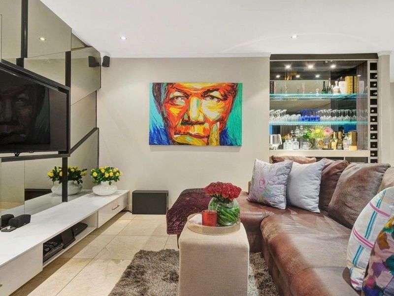A modern living room featuring tiled flooring, recessed downlights, a mirrored feature wall, and a built-in bar area with glass shelving.