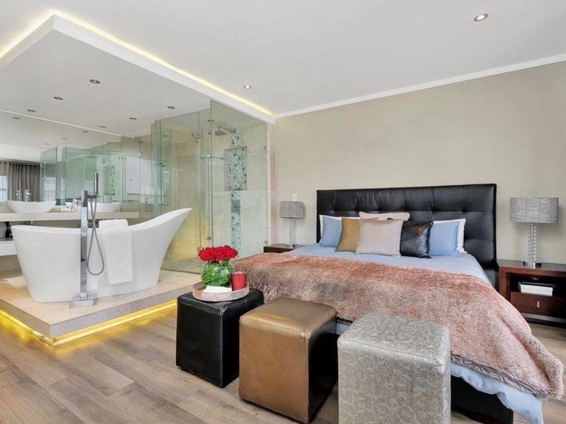 A modern open-plan bedroom featuring an integrated en-suite bathroom with a freestanding bathtub, glass shower, and premium finishes.