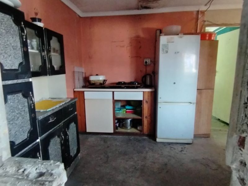 A kitchen space requiring significant renovation, featuring built-in cabinetry and a hob, with visible ceiling water damage and worn flooring throughout.