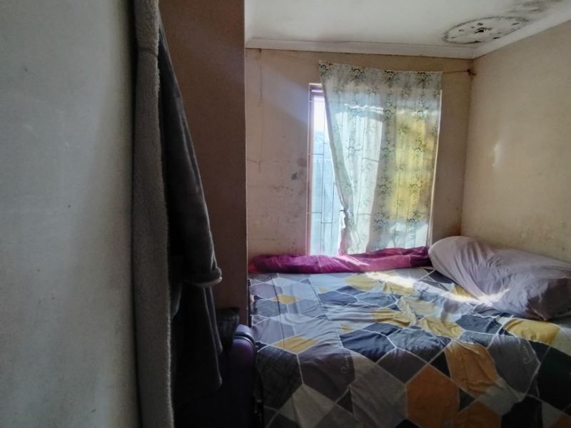 A bedroom featuring a window and ceiling detail, currently showing signs of significant wear including ceiling water damage and wall surface deterioration.