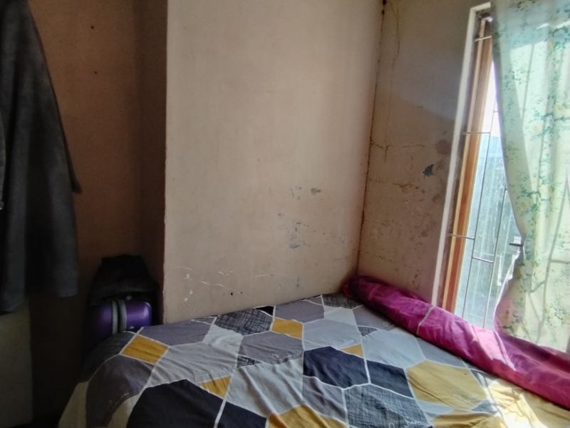 A bedroom featuring security bars on the window and coving, currently showing significant signs of wear including wall cracks and peeling paint.