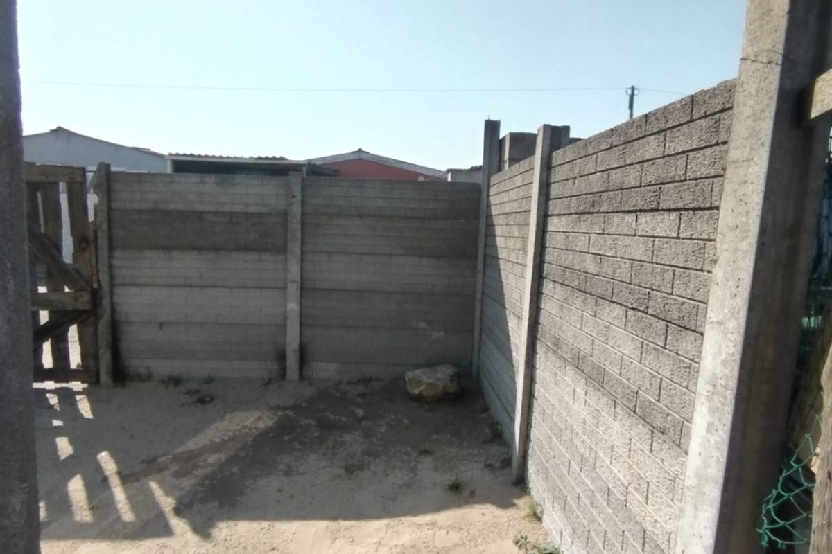A rear outdoor area enclosed by precast concrete boundary walls, featuring an unpaved sandy ground surface.