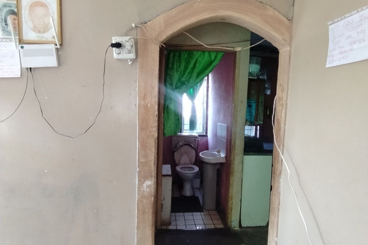 A small bathroom featuring a pedestal basin and toilet, accessed through an arched doorway from the adjacent living area.