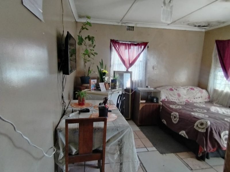 A bedroom featuring tiled flooring and ceiling panels, currently showing signs of significant wear including water damage and peeling paint on the ceiling.