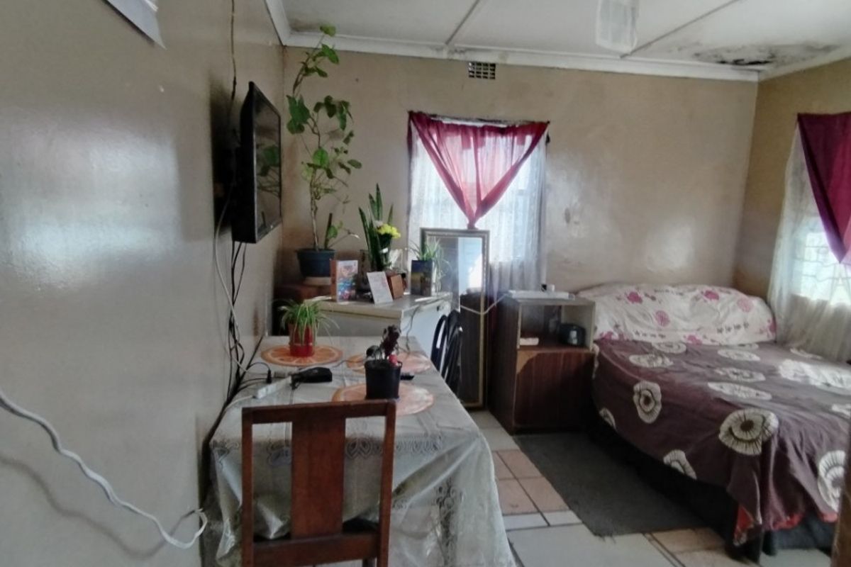 A bedroom featuring tiled flooring and ceiling panels, currently showing signs of significant wear including water damage and peeling paint on the ceiling.