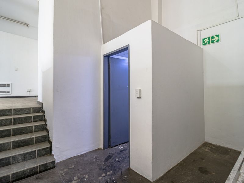 A functional commercial hallway featuring a staircase with tiled steps, an emergency exit sign, and a partitioned utility area.