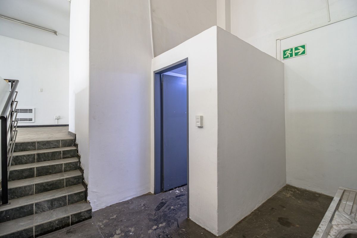 A functional commercial hallway featuring a staircase with tiled steps, an emergency exit sign, and a partitioned utility area.