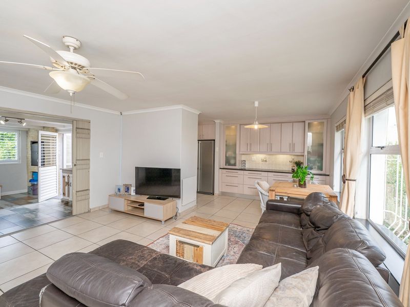 Spacious open-plan living area featuring tiled floors, a ceiling fan, and a functional kitchen with built-in cabinetry, seamlessly connecting to an adjacent patio space.