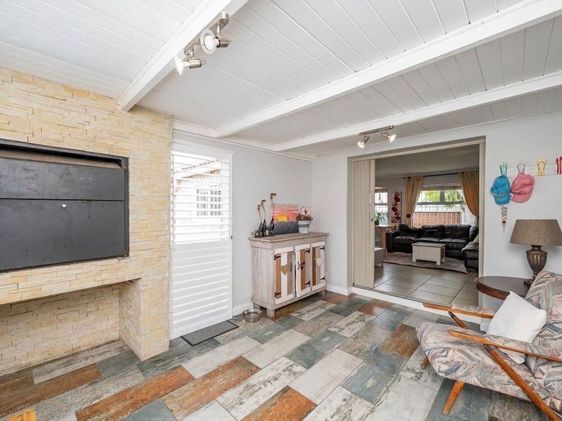 Covered patio area featuring a built-in braai with stone cladding, exposed beam ceiling, and decorative tiled flooring, providing seamless access to the main living space.
