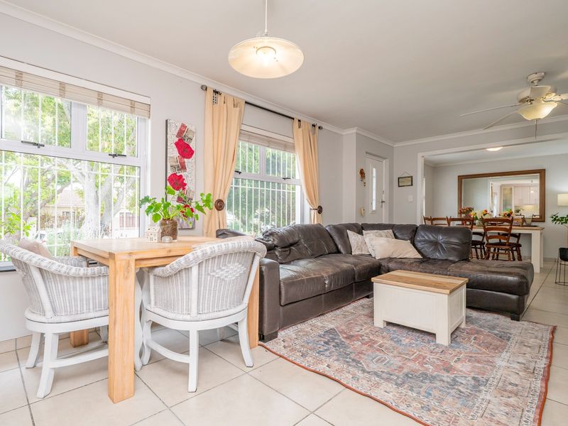 Spacious open-plan living area featuring tiled flooring, ceiling fan, and large windows with security bars, flowing into the adjacent dining space.