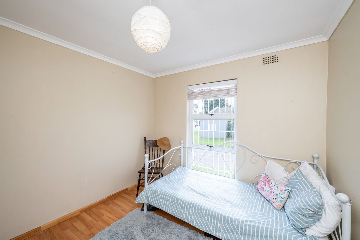 A functional bedroom featuring laminate flooring, a window with security bars, and neutral wall finishes, providing a comfortable and well-lit living space.