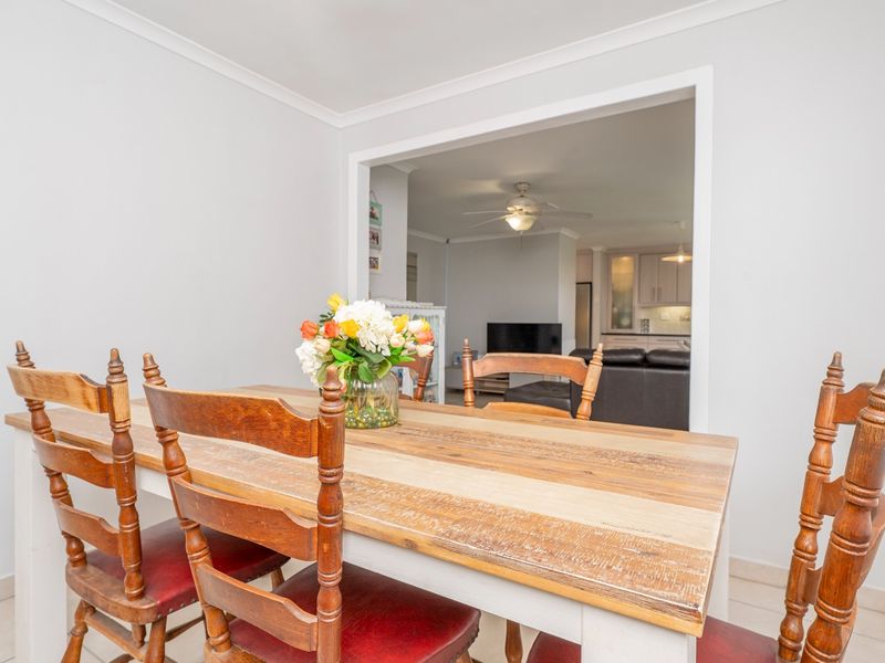 A dining room featuring tiled flooring and coved cornicing, with an open-plan view into the adjacent living area and kitchen.